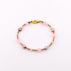 A beaded bracelet featuring a gold-tone lobster claw clasp, alternating between small metallic gold beads, round translucent pink beads, and irregular-shaped iridescent brown pearls, arranged in a circular pattern on a white background.