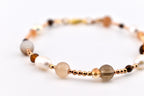 A beaded bracelet featuring a mix of white freshwater pearls, translucent beige and smoky quartz spheres, and small faceted amber-colored crystals, all interspersed with tiny metallic rose gold spacer beads on a thin cord.