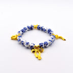 A beaded bracelet featuring round white beads with a blue floral pattern, interspersed with small gold-toned spherical spacers. The bracelet includes three gold-toned bow charms attached at intervals along the circular string of beads.