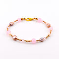 A beaded bracelet featuring alternating light pink round beads, metallic gold-toned spacer beads, small iridescent mauve pearls, and clear faceted crystals. The bracelet is secured with a gold-toned lobster claw clasp closure.