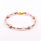A beaded bracelet featuring alternating light pink round beads, metallic gold-toned spacer beads, small iridescent mauve pearls, and clear faceted crystals. The bracelet is secured with a gold-toned lobster claw clasp closure.