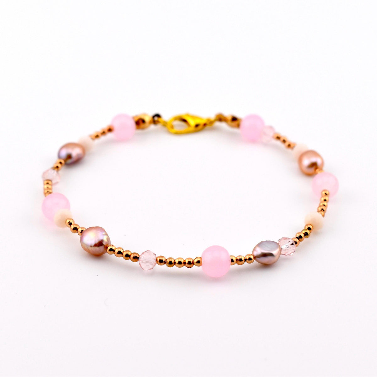 A beaded bracelet featuring alternating light pink round beads, metallic gold-toned spacer beads, small iridescent mauve pearls, and clear faceted crystals. The bracelet is secured with a gold-toned lobster claw clasp closure.