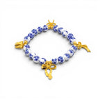 A beaded bracelet featuring round white beads with a blue floral pattern, interspersed with three polished gold-tone metal bow charms. The beads are arranged in a circular shape, creating a contrast between the blue and white ceramic-style beads and the metallic gold accents.