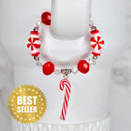 A circular beaded bracelet featuring red and white peppermint candy-shaped beads, clear faceted beads, and small silver-toned spacers. A single red and white striped candy cane charm hangs from the bottom of the bracelet.