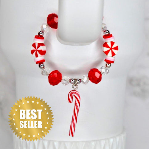 A circular beaded bracelet featuring red and white peppermint candy-shaped beads, clear faceted beads, and small silver-toned spacers. A single red and white striped candy cane charm hangs from the bottom of the bracelet.