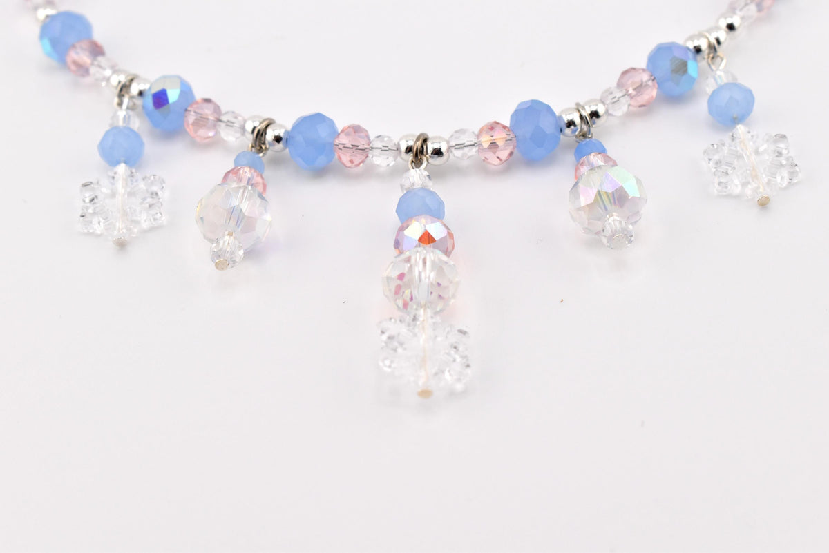 A necklace featuring a strand of light blue, pale pink, and clear faceted beads interspersed with silver-toned spacers. Five dangling charms, each composed of a clear snowflake-shaped bead and smaller round beads, hang from the main strand.