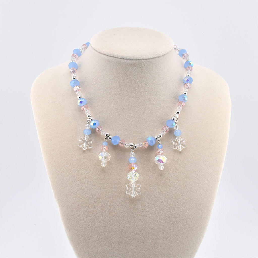 A necklace featuring light blue and pale pink faceted beads interspersed with small silver-toned spacers. The center of the necklace displays dangling charms, including clear acrylic snowflake shapes and iridescent crystal beads.