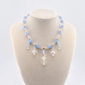 A necklace featuring light blue and pale pink faceted beads interspersed with small silver-toned spacers. The center of the necklace displays dangling charms, including clear acrylic snowflake shapes and iridescent crystal beads.