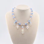 A necklace featuring light blue and pale pink faceted beads interspersed with small silver-toned spacers. The center of the necklace displays dangling charms, including clear acrylic snowflake shapes and iridescent crystal beads.