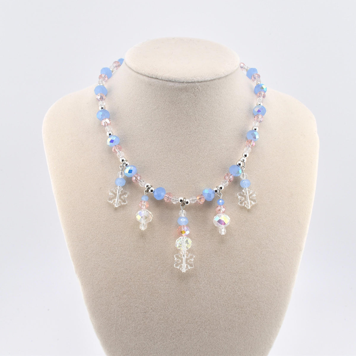 A necklace featuring light blue and pale pink faceted beads interspersed with small silver-toned spacers. The center of the necklace displays dangling charms, including clear acrylic snowflake shapes and iridescent crystal beads.
