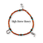A beaded bracelet featuring small orange and turquoise beads with three silver-toned charms: a cactus, a horseshoe, and a cowboy boot. The text High Horse Honey is centered within the circular arrangement of the beaded jewelry piece.