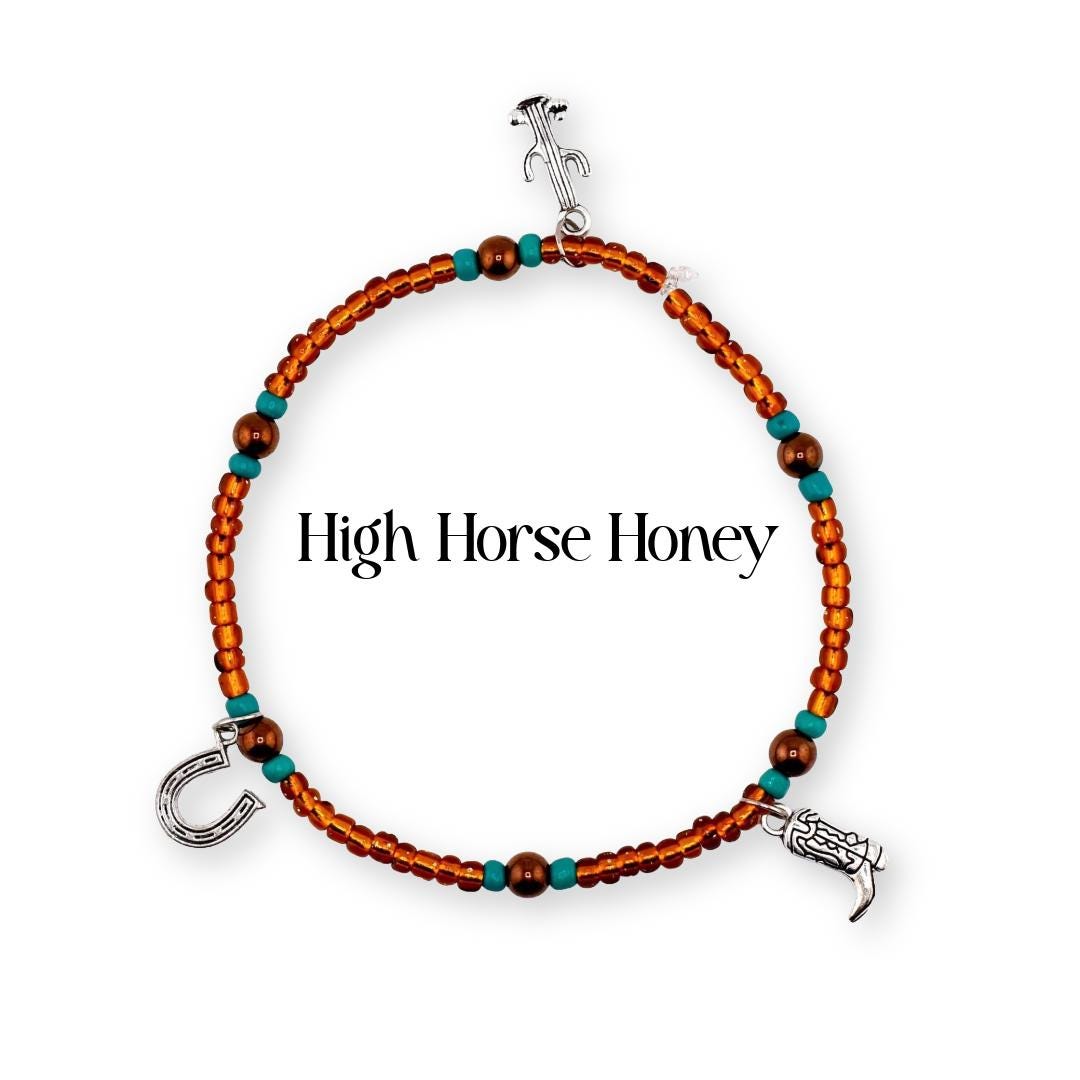 A beaded bracelet featuring small orange and turquoise beads with three silver-toned charms: a cactus, a horseshoe, and a cowboy boot. The text High Horse Honey is centered within the circular arrangement of the beaded jewelry piece.