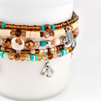 A multi-strand beaded bracelet featuring brown, beige, and turquoise beads in various shapes and textures. The bracelet includes silver-toned metal charms shaped like a cowboy boot and a horse head, interspersed among the beads.