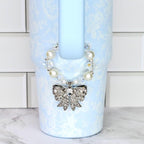 A light blue Stanley with a floral pattern and a decorative bow. The bow is silver with clear rhinestones. The tumbler has a pearl and crystal beaded strap.