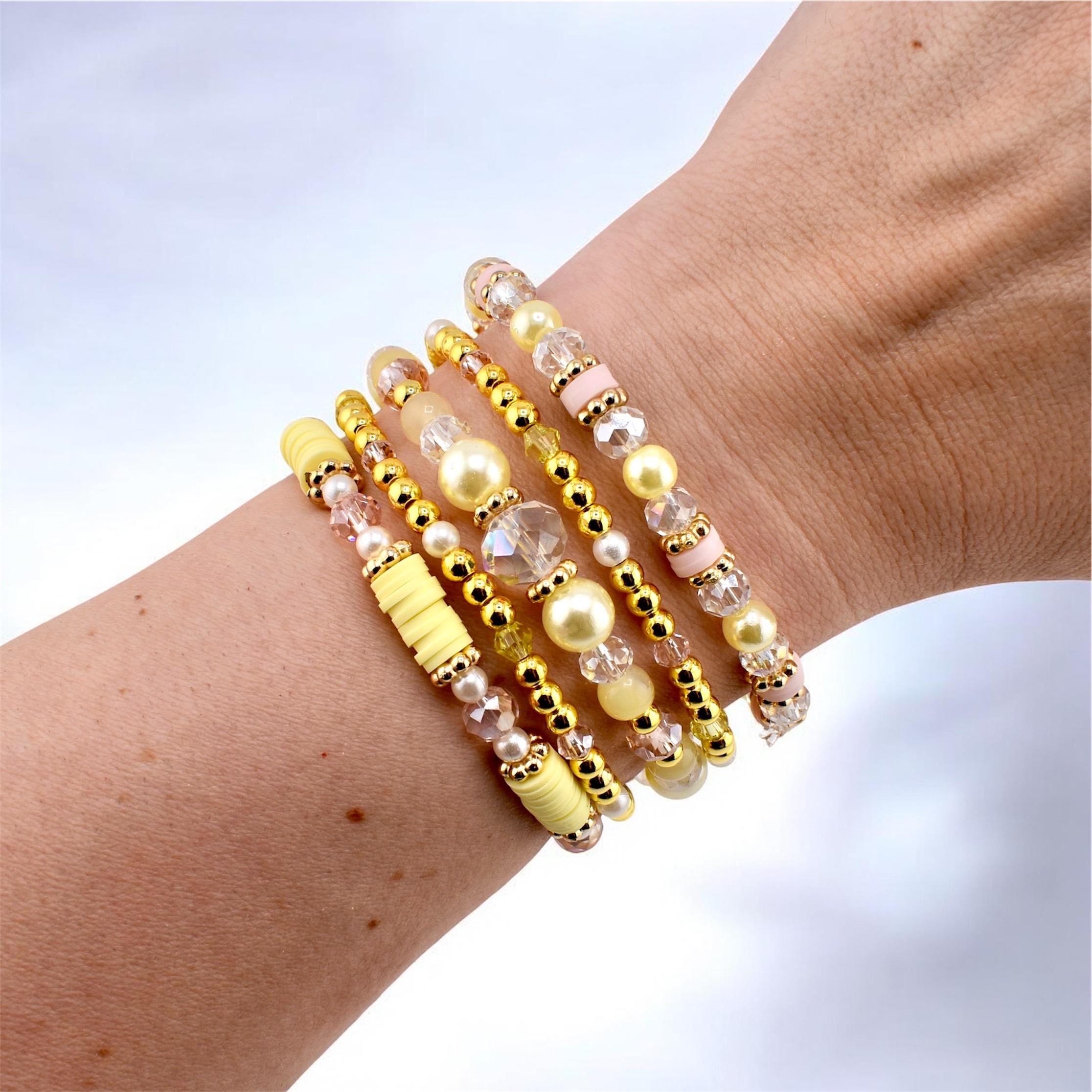 A stack of five bracelets featuring a mix of yellow clay heishi beads, gold-toned metallic spacer beads, clear faceted crystal beads, and smooth pale yellow and soft pink round beads arranged in a layered, multi-textured design.