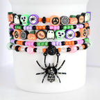 Stack of 5 colorful Halloween beaded tumbler bracelets with spooky charms including spiders, ghosts, pumpkins, skulls, and ‘boo’ text beads in black, orange, green, purple, and pink; features rhinestone spider charm centerpiece.