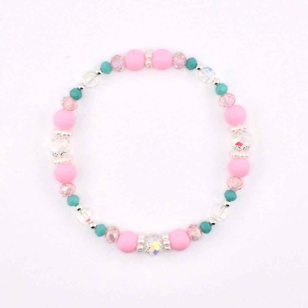 A circular beaded bracelet featuring a repeating pattern of matte pink round beads, small teal round beads, clear faceted crystal beads, and tiny white spacer beads arranged in a symmetrical design on a flexible elastic cord.