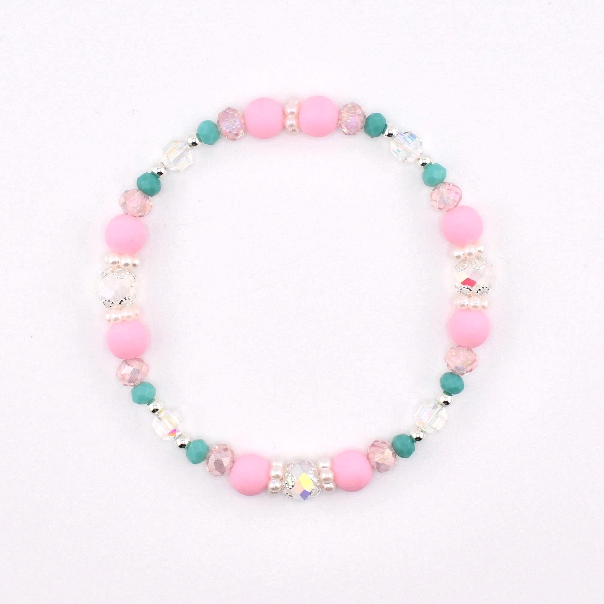 A circular beaded bracelet featuring a repeating pattern of matte pink round beads, small teal round beads, clear faceted crystal beads, and tiny white spacer beads arranged in a symmetrical design on a flexible elastic cord.