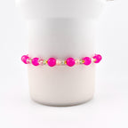 A beaded bracelet featuring vibrant hot pink round beads alternating with smaller, clear faceted crystal beads and tiny gold-toned metallic spacers. The design is symmetrical, showcasing a repeating pattern of pink and clear elements.