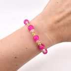 A beaded bracelet featuring alternating round hot pink beads, clear faceted crystal beads, and small metallic gold spacer beads. The bracelet is constructed with a flexible cord and displays a repeating pattern of these colorful elements.