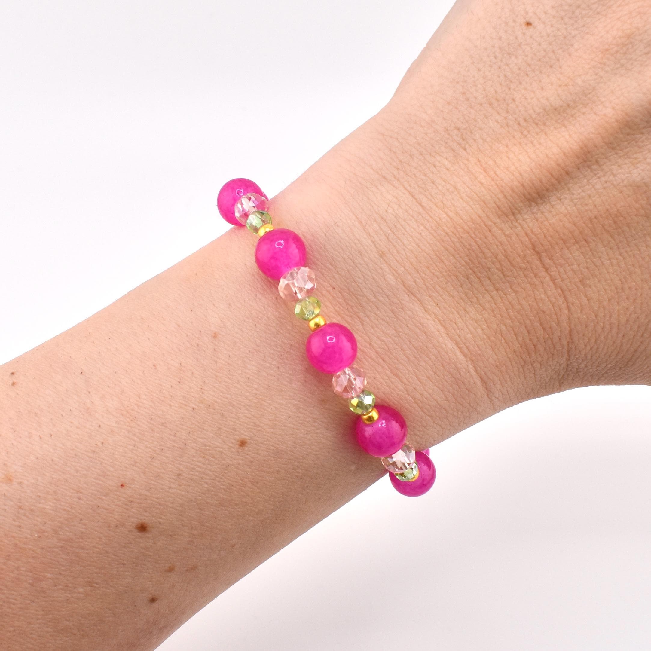 A beaded bracelet featuring alternating round hot pink beads, clear faceted crystal beads, and small metallic gold spacer beads. The bracelet is constructed with a flexible cord and displays a repeating pattern of these colorful elements.