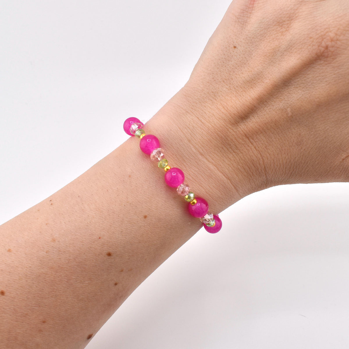 A beaded bracelet featuring round, vibrant hot pink beads alternating with smaller, clear faceted crystal beads and tiny lime green spacer beads. The bracelet is constructed with a flexible cord and displays a repeating pattern of pink and clear elements.