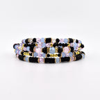 A multi-strand bracelet featuring a combination of black disc beads, light blue round beads, faceted clear crystals, and small gold-toned metallic spacers. The design incorporates alternating textures and colors arranged in a layered pattern.
