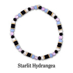 A circular beaded bracelet featuring alternating segments of black disc beads, light blue round beads, faceted lavender beads, and white beads, accented with small gold-toned spacers. The text Starlit Hydrangea is printed below.
