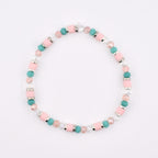 A beaded bracelet featuring a repeating pattern of cylindrical light pink beads, round turquoise beads, faceted clear crystal beads, and small silver-toned metal spacers arranged in a circular design on a plain white background.
