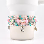 A stack of five beaded bracelets featuring pastel pink and turquoise clay discs, clear faceted beads, and round pink beads. Silver charms include a ghost, a spider, a spiderweb, an owl, and a bat, all strung on elastic cord.
