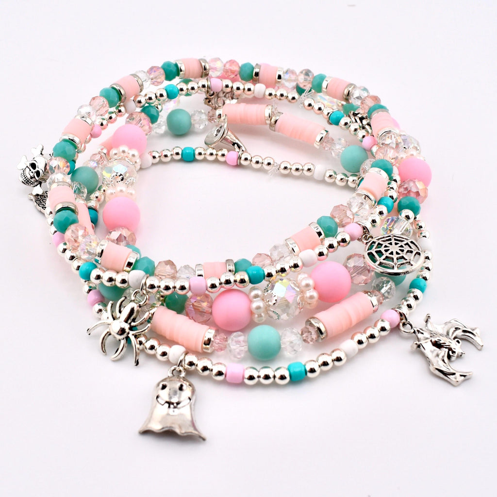 A stack of beaded bracelets featuring pink, turquoise, and clear faceted beads, interspersed with silver-toned metallic beads. The bracelets include silver charms shaped like a skull, a spider, a ghost, a spiderweb, and a bat.