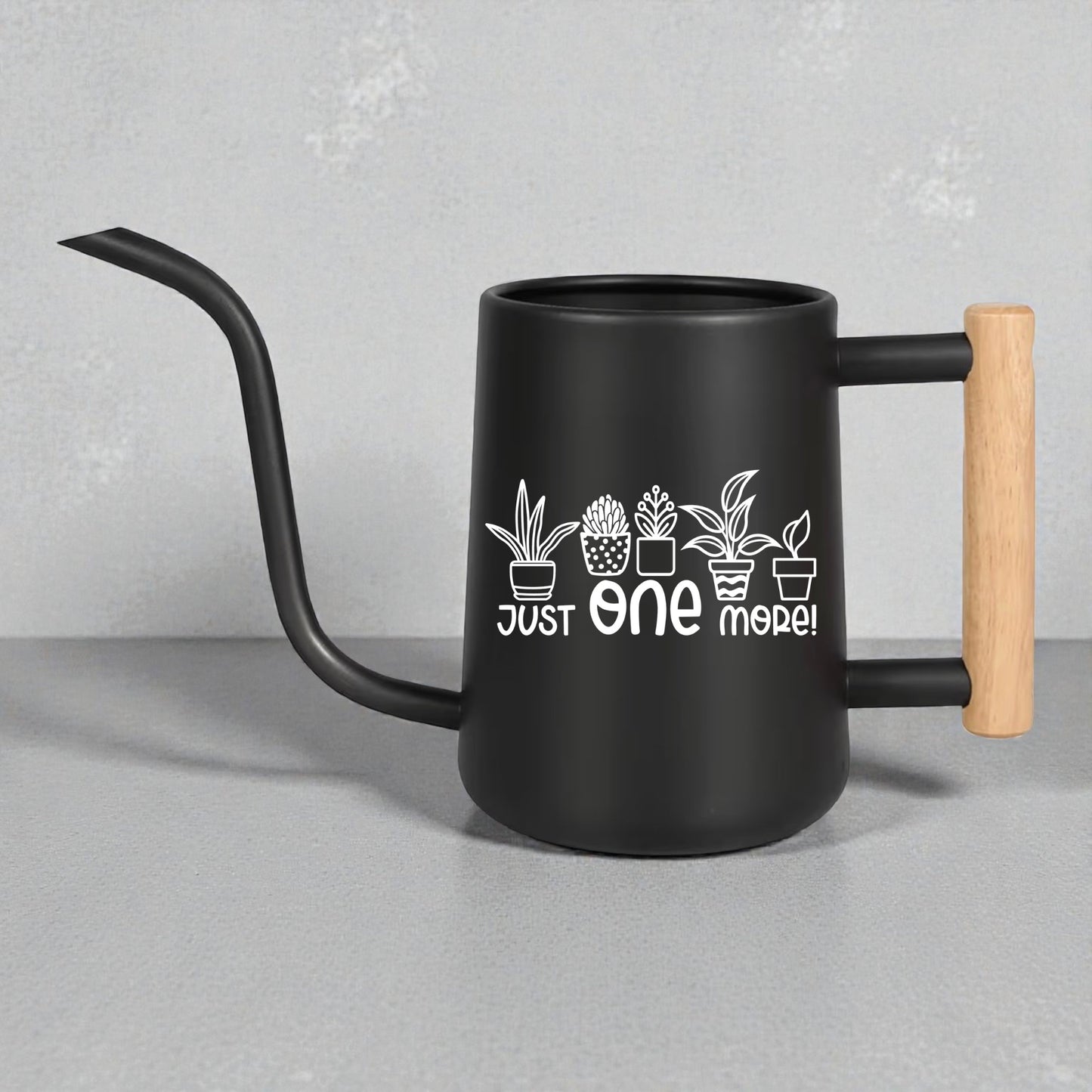 Black watering can with wooden handle and plant designs on a gray background