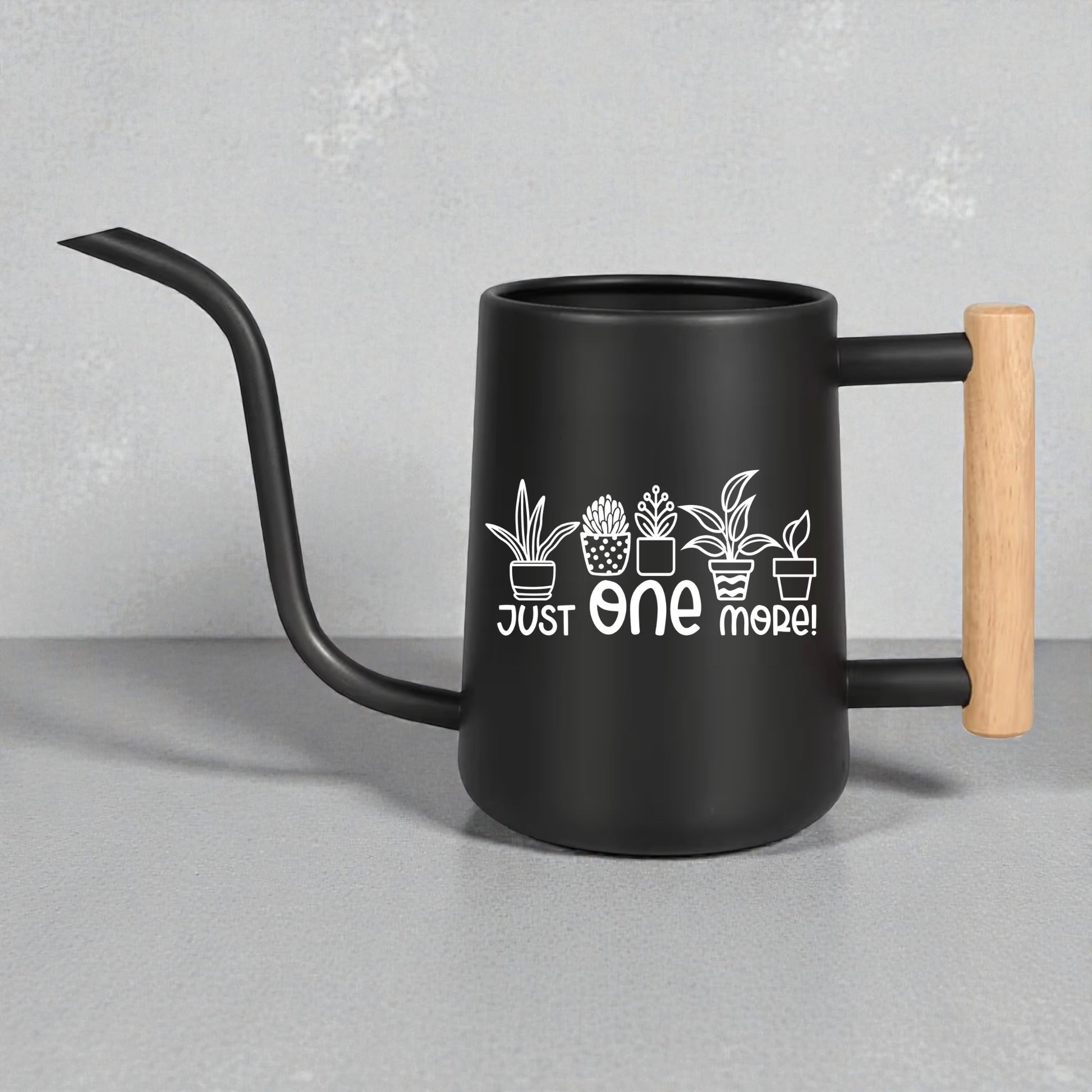 Black watering can with wooden handle and plant designs on a gray background