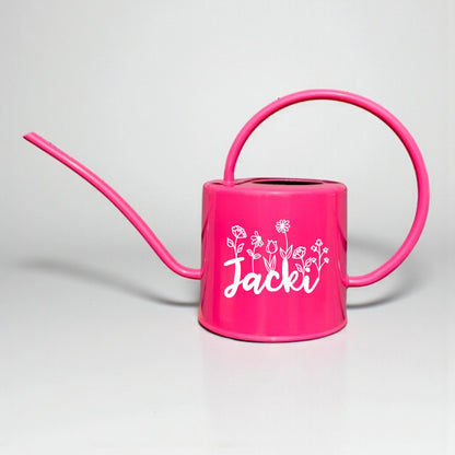 Pink watering can with a name and floral designs on a light gray background