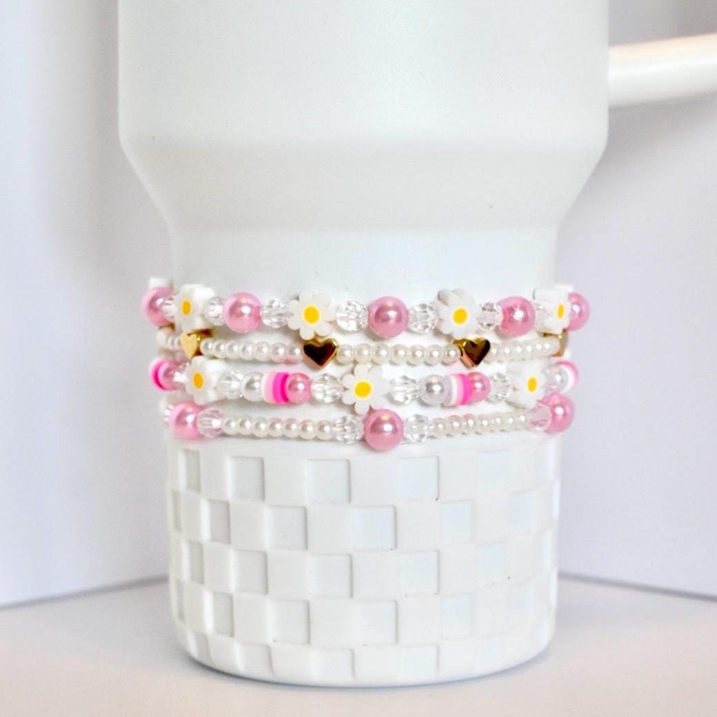 Set of beaded bracelets with pink and white pearls and daisy clay bead accents on a white Stanley tumbler