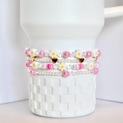 Set of beaded bracelets with pink and white pearls and daisy clay bead accents on a white Stanley tumbler