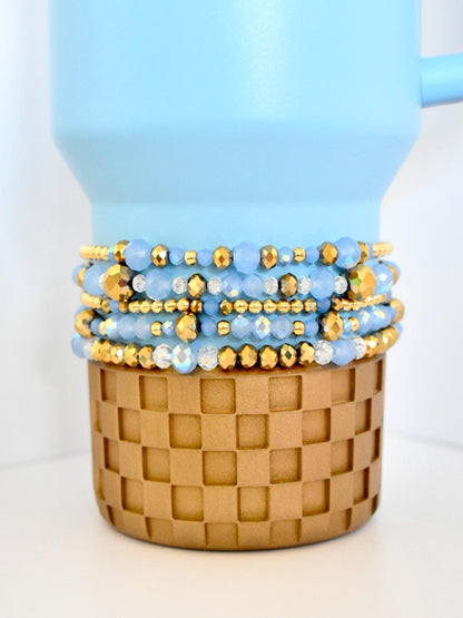 Set of blue and gold beaded bracelets on a woven basket with a light blue background