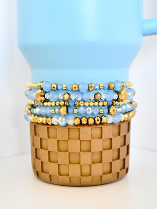 Set of blue and gold beaded bracelets on a woven basket with a light blue background